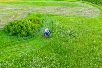 Aerial top view farm scene agricultural tractor mows grass with a mower in the farm fields, haymaking.
