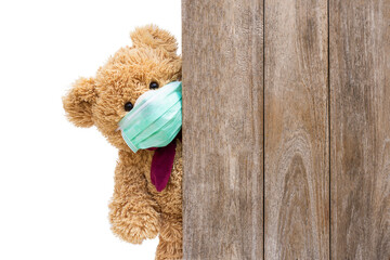 Brown sick teddy bear with protective medical mask behind the old wooden door or window. Stay at home quarantine coronavirus pandemic prevention, covid-19 concept.