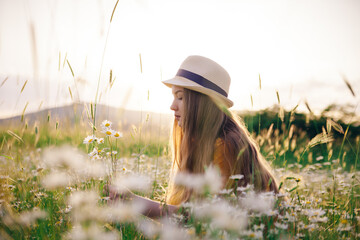 A young girl in a straw hat gathering flowers on the summer field