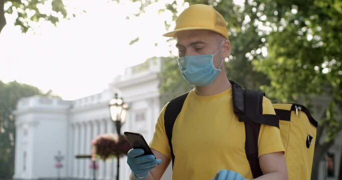 The guy from the delivery service received an order on his smartphone for food delivery. Masked and gloved delivery man in food delivery service.
