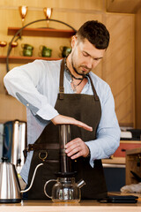 Aeropress coffee: barista press to device and coffee drops pours trought aeropress to pot. Alternative coffee brewing method. Vertical photo handsome bearded barista makes tasty Scandinavian coffee