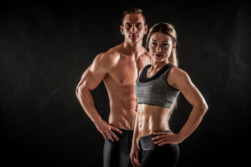 Fototapeta na wymiar Fitness in gym, sport and healthy lifestyle concept. Couple of athletic man and woman showing their trained bodies on black background. Two bodybuilder models standing and demonstrating tight muscles.