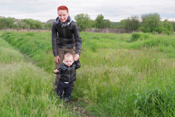 Mom with a little boy walks in the park. Red-haired woman with a small child. Mom and son in black leather jackets.