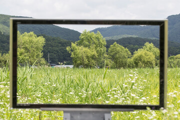 steel square photo frame against green field and mountain.