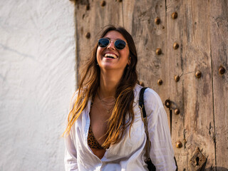 A young caucasian female in sunglasses smiling while posing in front of a wooden wall