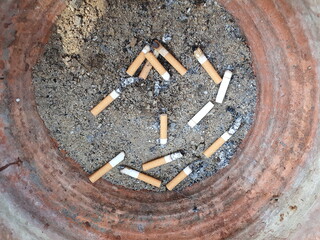 Many cigarette butts burnt with ashes are thrown into the ashtray made of clay and sand inside....
