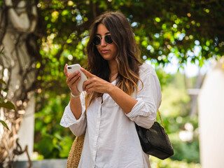 A young caucasian female smiling and using her phone while walking in the street