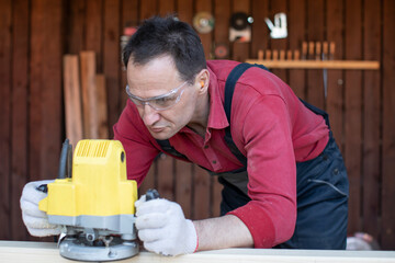 Handsome 40s carpenter works on wooden workpiece with milling tool at cottage workshop close up. Processing of Natural Wooden beam with milling woodworking machine. jack of all trades concept