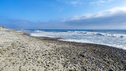 Sea, beach boulders, pebble shore and waves at sunset. Sea waves breaking on rocks. Sunny beach with sand dunes and blue sky in Esposende, Portugal.