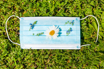 used doctor's protective mask with flowers on green grass, the end of the virus epidemic