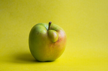 Funny, ugly apple isolated on a yellow background. Image with copy space, horizontal orientation, side view.
