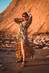 Fototapeta na wymiar Summer lifestyle on a beach next to rocks of a young brunette Caucasian woman in a leopard dress by the sea. Sakoneta beach in the town of Deba, Basque Country.