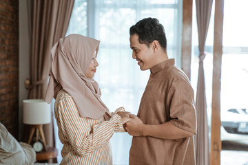 young Muslim couple smiling happily facing each other holding hands while standing in the room