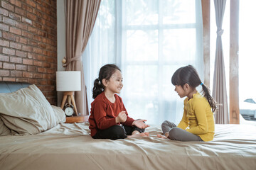 Obraz na płótnie Canvas two little girls smiled happily playing together when sitting on the bed in the room