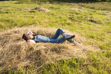 Naklejka na ściany i meble A young woman or teenage girl is lying on the hay, dreaming, resting. Holidays, summer mood, Sunny summer day.