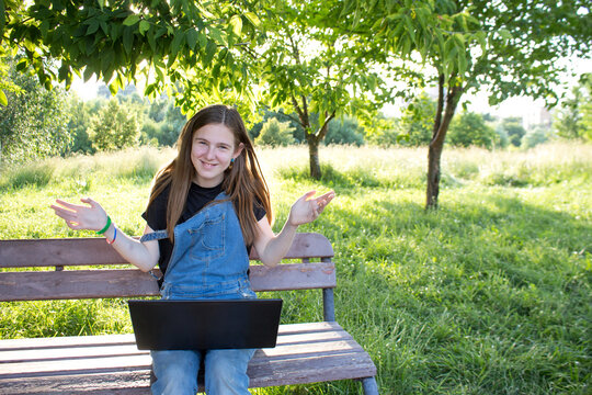 A young woman or teenage girl with a leptop on a bench is  surfing the Internet or studying outdoors. Holidays, summer mood, Sunny summer day.