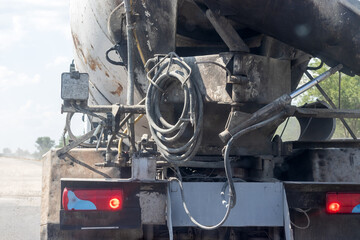 Concrete mixer truck rear view with hoses and burning taillights during road works on an intercity highway. Closeup view