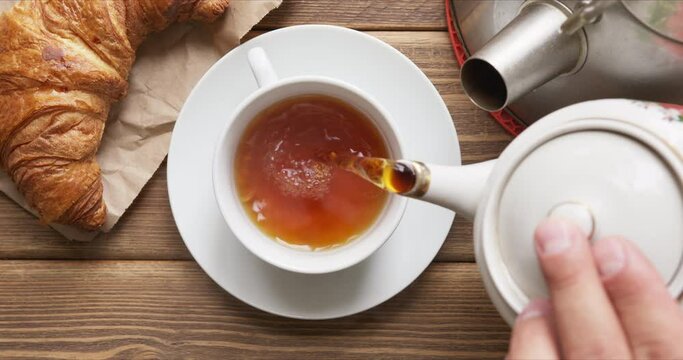 Top view of person pours hot fresh black tea in a mug