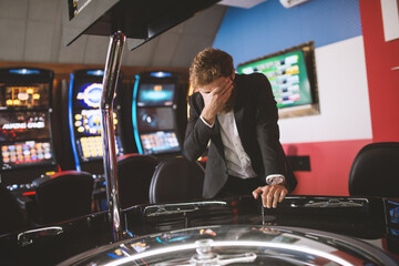 young man in a modern black suit stands next to a roulette machine and gets upset about the money lost at roulette