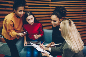 Young hipster girls fill in forms of registration to business courses using modern technology,group of international female students writing answers to questionnaire while spending time together