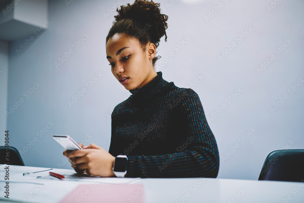 Poster pensive african american hipster girl checking notification on cellular while sitting in classroom, 
