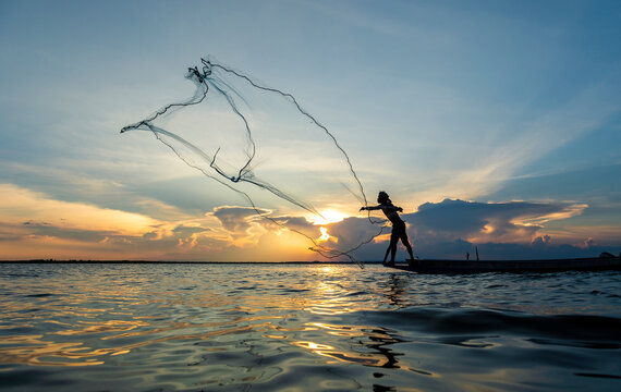 Fisherman throwing net fishing on boat in the lake at sunset.