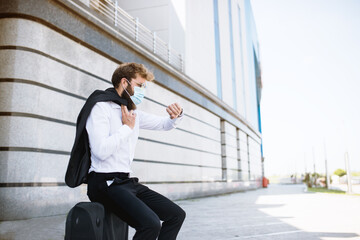 young businessman with a mascot on his face that prevents the spread of a pandemic caused by the corona virus goes on a trip to another country and watches the time on his watch he wears on his hand