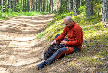 man sitting on dirt road in pine and spruce forest, hiking trip with dog. Solo outdoor activities. Enjoy time alone in nature.