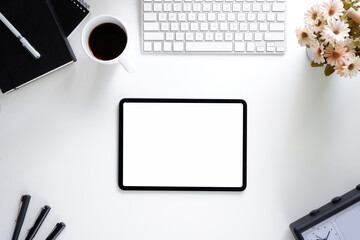 Office desk table with tablet,coffee cup ,pencil ,flower ,notepad on white desk. Top view with copy space.