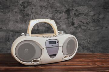 White cassette tape radio and cd-dvd player on wooden table in front of concrete wall background.