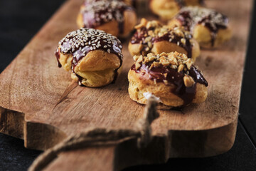 Choux pastry. Profiteroles with butter cream garnished with chocolate sauce, nuts and sesame seeds.