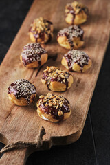 Choux pastry. Profiteroles with butter cream garnished with chocolate sauce, nuts and sesame seeds.