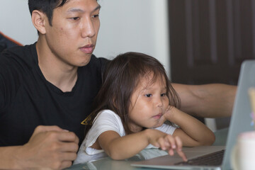 Young asian dad teaching his young daughter how to use a laptop computer at home. Home-school and education.