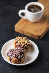 Choux pastry. Profiteroles with butter cream garnished with chocolate sauce, nuts and sesame seeds. Dessert and coffee for breakfast.