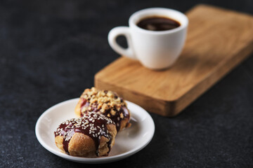 Choux pastry. Profiteroles with butter cream garnished with chocolate sauce, nuts and sesame seeds. Dessert and coffee for breakfast.