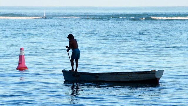 Fisherman on pirogue (boat) on tropical sea in silhouette - Mauritius