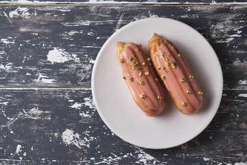 Eclairs in a plate. Dessert on an old wooden table. Choux pastry dessert with peanut fondant and golden sugar beads.