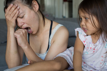Tired restless young mother yawning while taking care of her cute worried daughter. Single parent and maternity life.