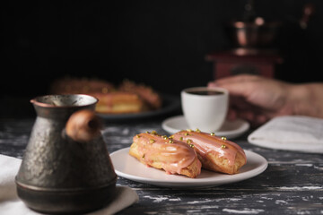 Espresso and eclairs for breakfast. Tasty cream cakes on the kitchen wooden table.