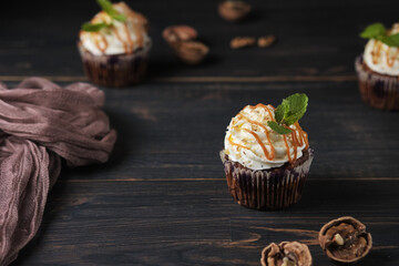 Carrot cupcakes stuffed with caramel and walnuts. Cupcakes with cream cheese cream and icing sugar. The dessert is decorated with mint and caramel.