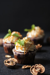 Carrot cupcakes stuffed with caramel and walnuts. Cupcakes with cream cheese cream and icing sugar. The dessert is decorated with mint and caramel.