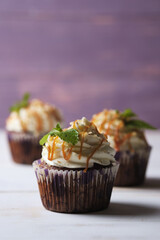 Carrot cupcakes stuffed with caramel and walnuts. Cupcakes with cream cheese cream and icing sugar. The dessert is decorated with mint and caramel.
