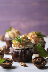 Carrot cupcakes stuffed with caramel and walnuts. Cupcakes with cream cheese cream and icing sugar. The dessert is decorated with mint and caramel.
