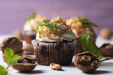 Carrot cupcakes stuffed with caramel and walnuts. Cupcakes with cream cheese cream and icing sugar. The dessert is decorated with mint and caramel.