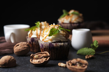 Carrot cupcakes stuffed with caramel and walnuts. Cupcakes with cream cheese cream and icing sugar. The dessert is decorated with mint and caramel.