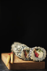 Sushi on a wooden board. Rolls with fish on a dark background.