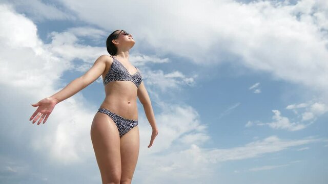 Slim brunette girl in sunglasses smiling and sunbathing on an airy sea beach
