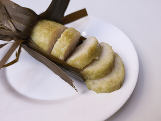 Lontong is an Indonesian dish made of compressed rice cake in the form of a cylinder wrapped inside a banana leaf. Cut into slices. Isolated in white background.