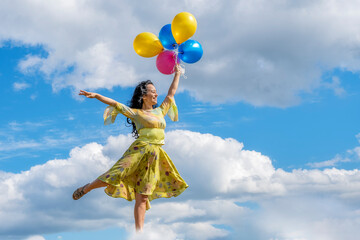 Beautiful and happy girl in a green dress flies on balloons in the clouds of blue sky