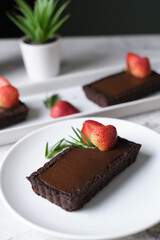 Rectangular chocolate tart with strawberry in white plate set in cafe table.